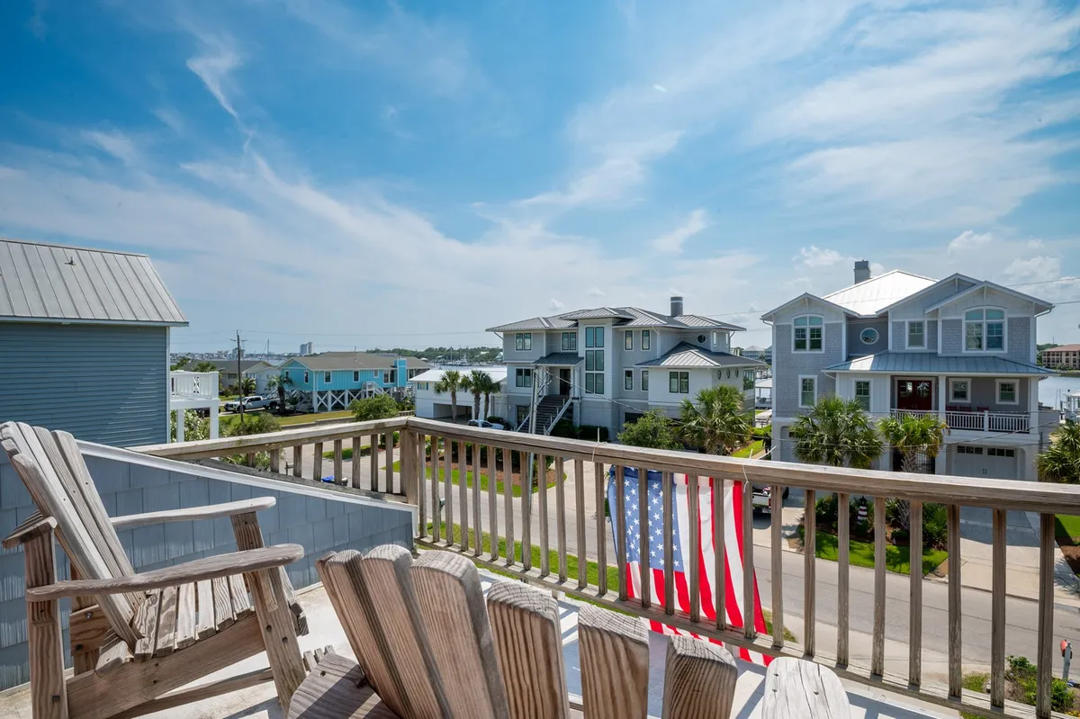 Adirondack chairs rest on a deck overlooking the Intracoastal Waterway, with an American flag and neighboring houses visible in the background. The scene is inviting, highlighting opportunities for relaxing, socializing, and taking in water views after a day out with your dog.