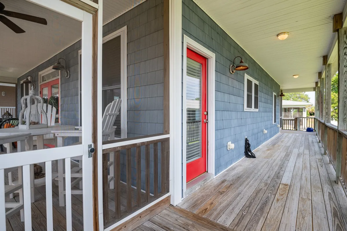 A welcoming interior view showcasing a red door leading to a screened porch with a wooden floor and outdoor seating. The transition from indoors to the porch is clear, emphasizing the easy flow between indoor and outdoor spaces. The porch area offers views perfect for relaxation.