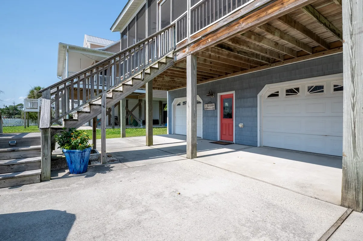 A bright exterior scene showcasing a staircase leading to an upper deck, a cheerful coral door, and a blue flower pot. The porch offers a great spot for gathering and enjoying the outdoors.