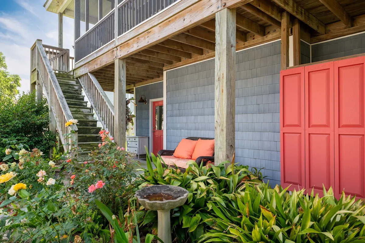 A charming exterior view featuring a welcoming staircase, a vibrant flower garden, a cushioned bench, and a birdbath. The landscaped setting conveys a sense of relaxation and an inviting atmosphere for both people and pets.