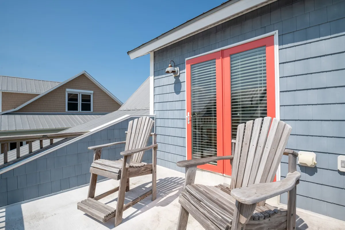 An exterior scene with wooden chairs set against a blue siding and a prominent red door, this spot offers a tranquil place to relax and enjoy the view. The scene suggests stargazing or sunset watching, with a sense of peace that ties into the natural beauty of the area.