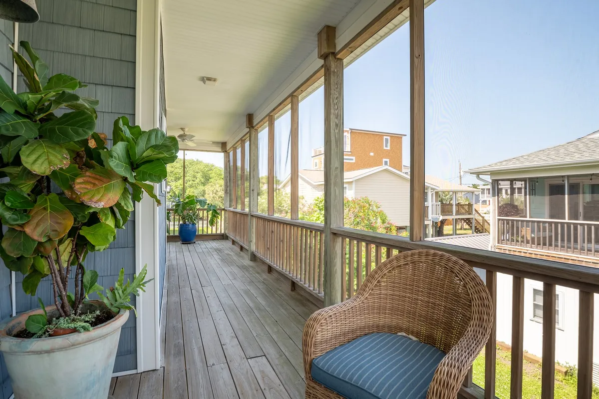 This image features a serene exterior space with a screened porch, a wicker chair, and a potted plant. The porch overlooks natural surroundings and invites guests to relax and enjoy the calming atmosphere, perfect for watching a sunrise or unwinding in the evening.