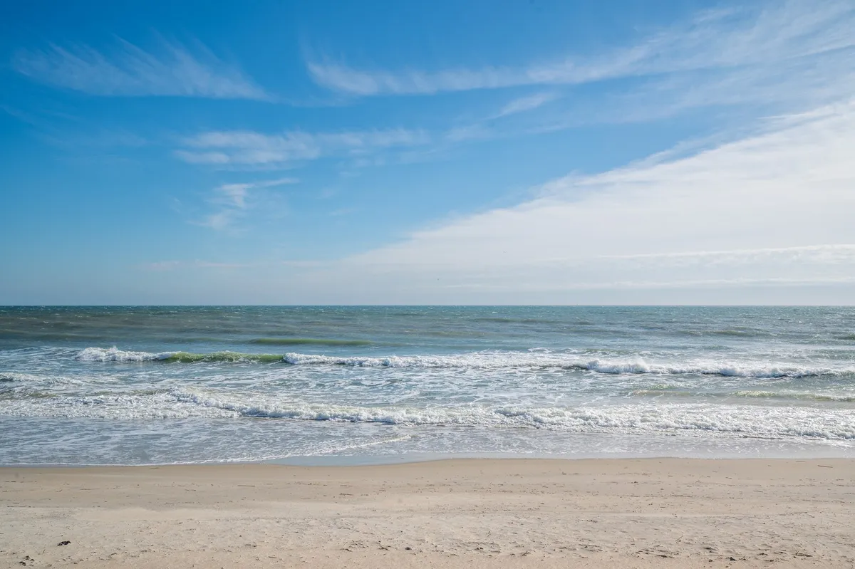A panoramic view of ocean waves, sandy beach, and blue sky, exuding tranquility and endless possibilities for walks, play, and relaxation.
