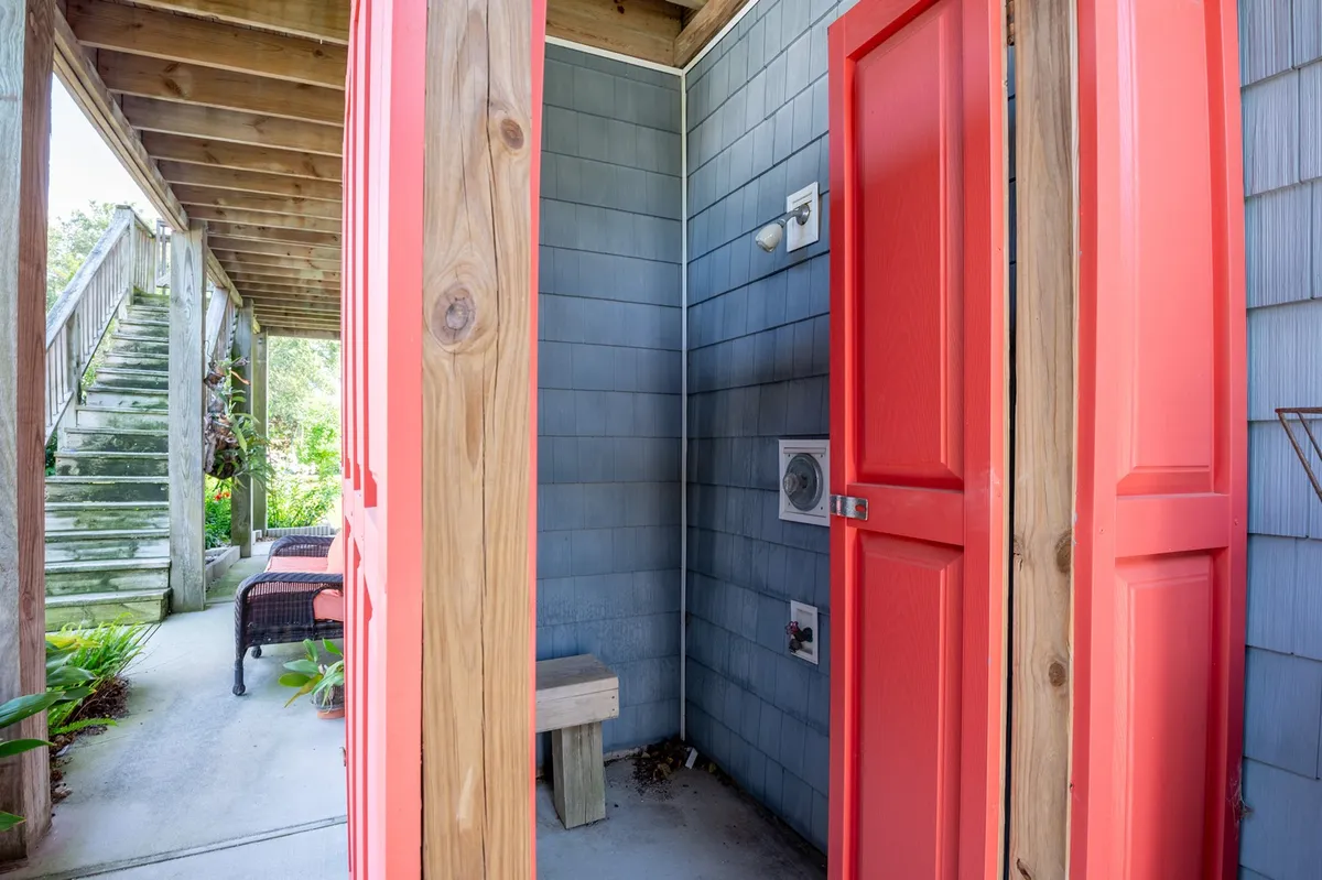 A playful, colorful space with bright red doors and textured blue siding, featuring a wooden bench. The area is set up for casual conversation and includes a spot for outdoor showers, evoking a beachy, fun vibe.