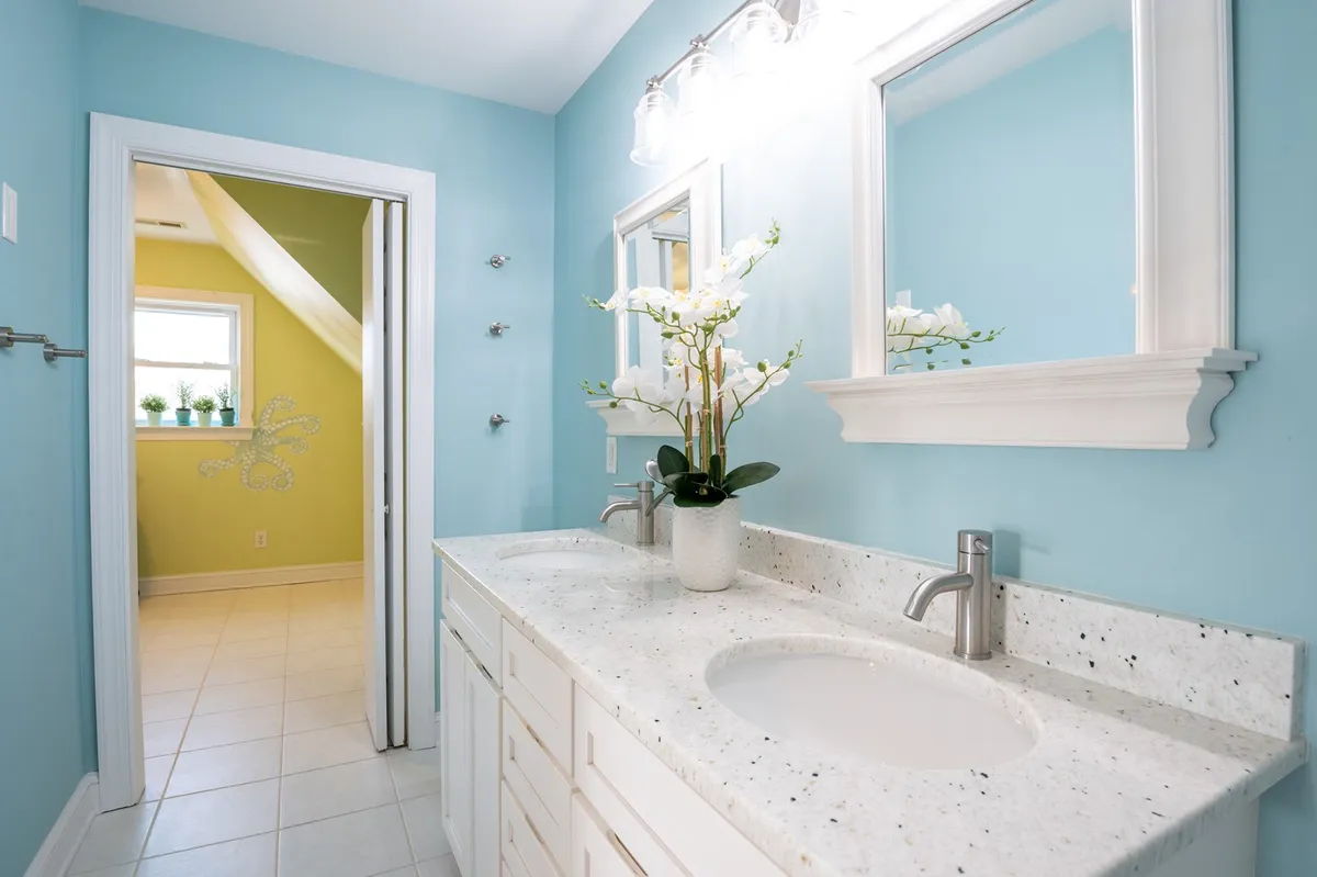 A bright and calming bathroom with a double vanity, two mirrors, and a plant arrangement. The space feels accessible and thoughtfully designed for convenience and self-care routines.