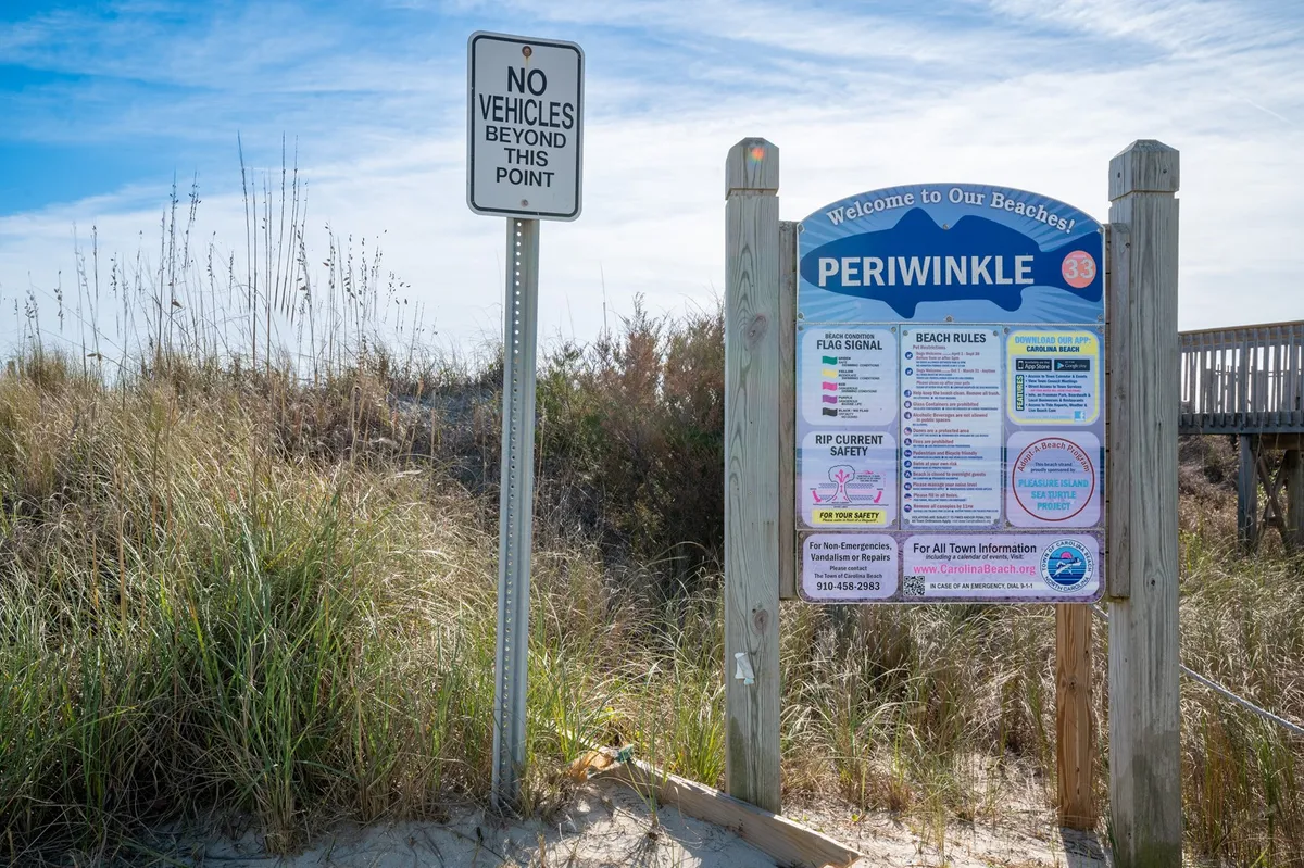 A welcoming exterior shot with a beach access sign, grassy dunes, and open sky, inviting families to explore the shoreline and enjoy sunny adventures.