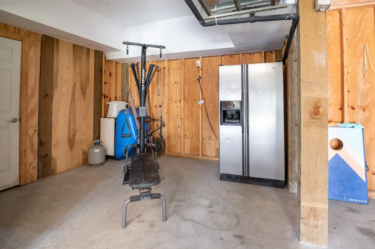 A practical interior space showcasing exercise equipment alongside a refrigerator, set against wooden walls. The room is functional, offering both fitness and convenience elements in one view.