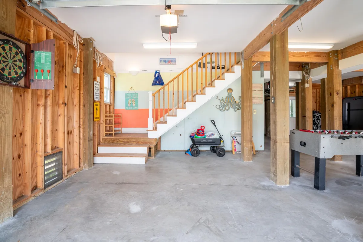 A vibrant interior game area featuring a foosball table, dartboard, staircase, and a playful octopus mural painted on the wall. The space is bright and energetic, clearly designed for friendly competition and family fun.